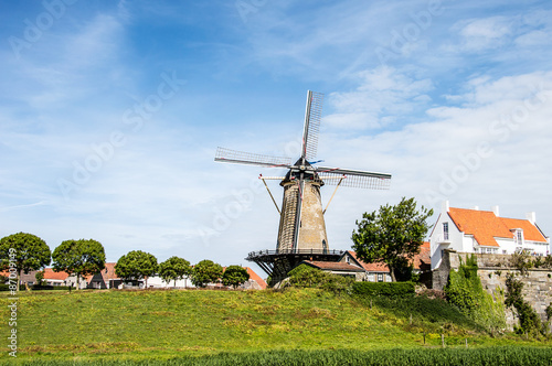 A typical Dutch landscape with a mill and little houses, blue sky, green grass and trees in Zeeland, the Netherlands