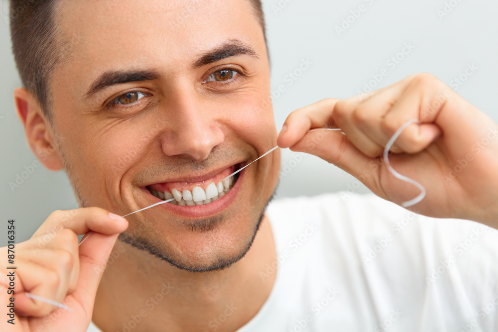 Closeup of young man flossing his teeth. Cleaning teeth with den - obrazy, fototapety, plakaty 