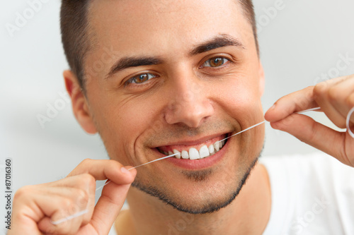 Closeup of young man flossing his teeth. Cleaning teeth with den