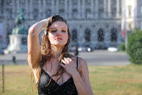 Young woman takes a refreshment under a sprinkler on a hot summer day