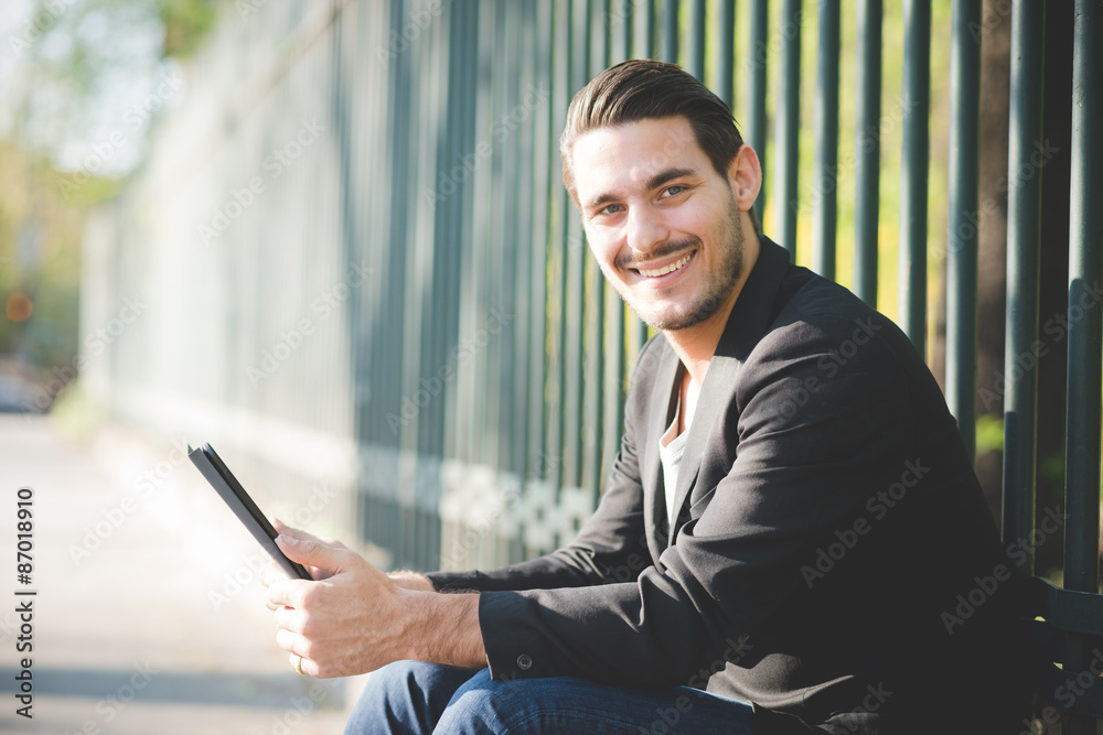 Fototapeta premium Young italian boy seated on a sidewalk using tablet