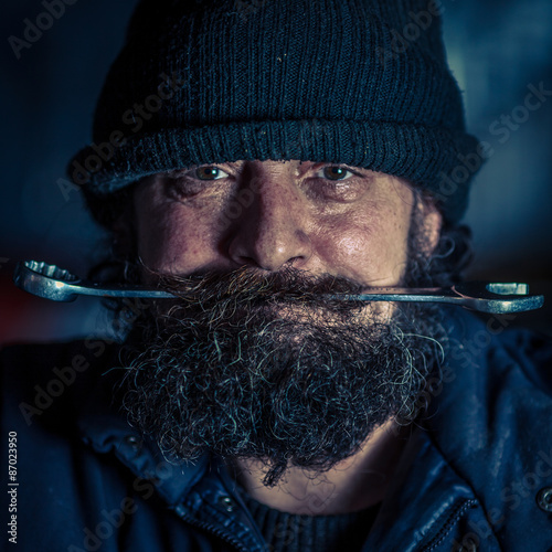 Portrait of mechanic with beard holding steel wrench in mouth