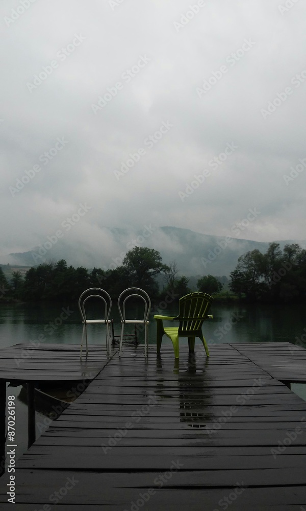 Rainy summer day, river lake dock, chairs and mountain view