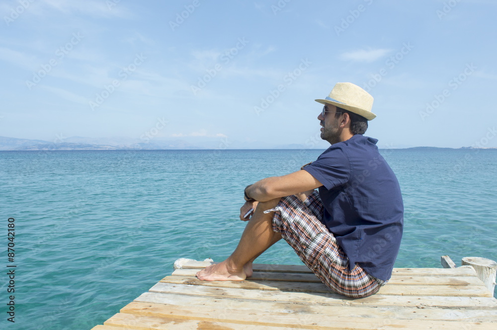 Young man sitting on the dock looking at blue sea