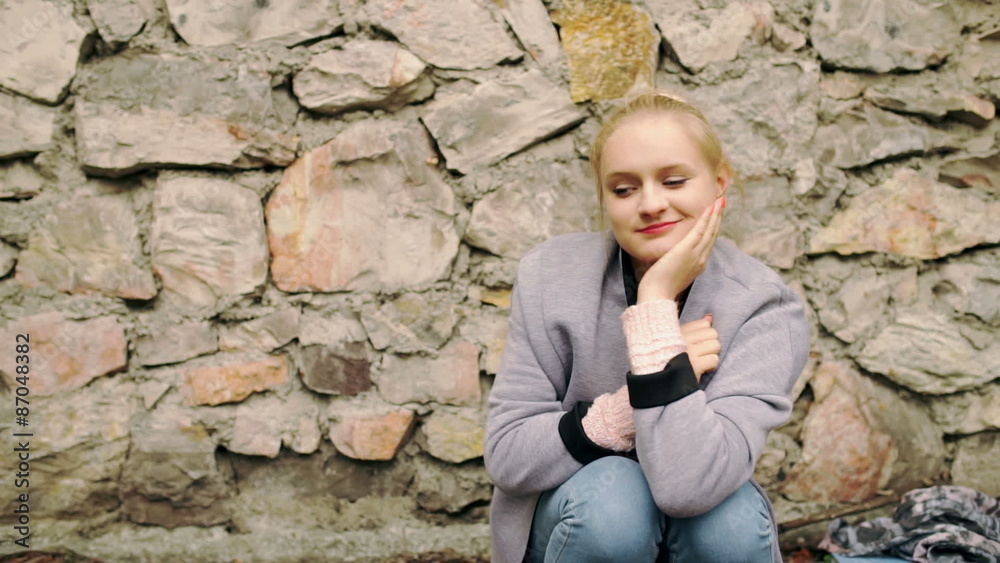 Dreaming girl sitting alone and smiling next to the brick wall
