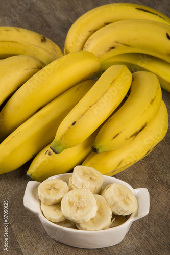 A banch of bananas and a sliced banana in a pot over a table.