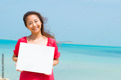 沖縄の海をバックにホワイトボードをもつ女性(3)
