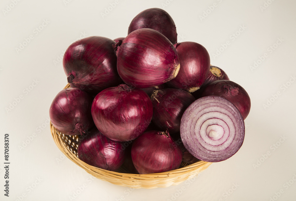 Obraz premium Red onions in a basket and a cut red onion over a table.