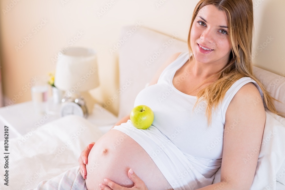 Pregnant woman lying on bed with apple in belly Pregnant woman lying on bed with apple in belly