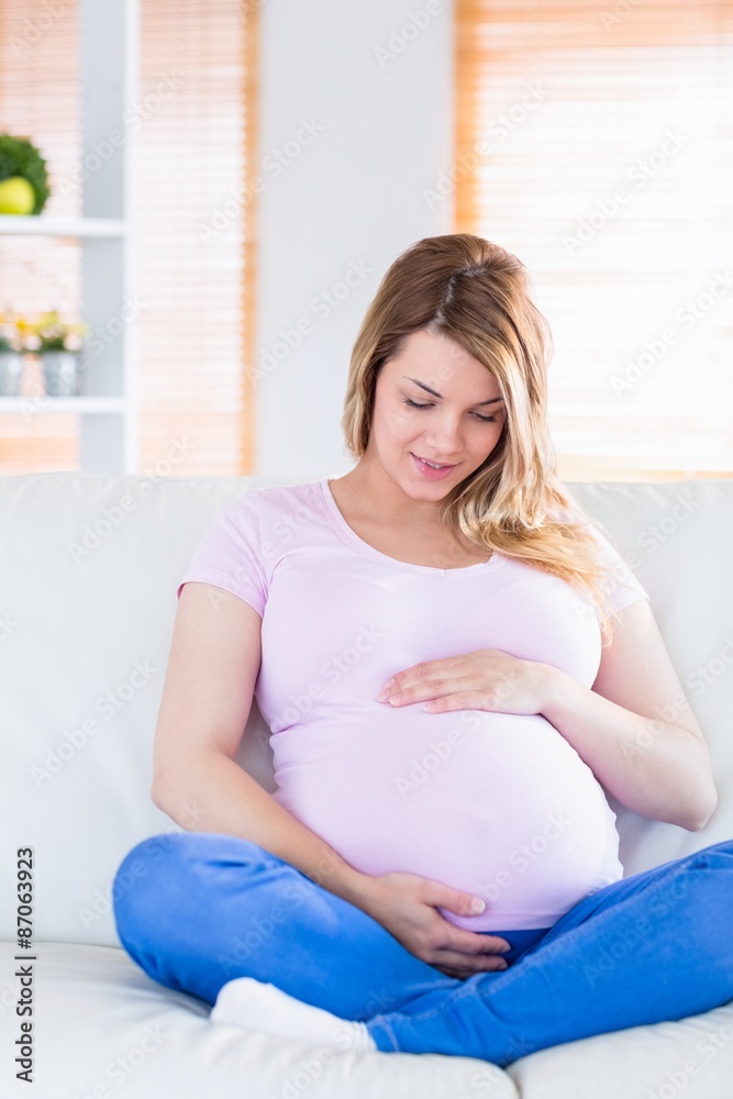 Pregnant woman sitting on couch touching her belly Pregnant woman sitting on couch touching her belly