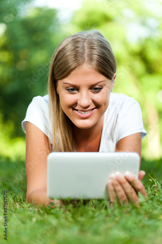 Young woman lying in grass and using digital tablet