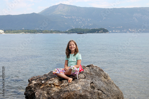 happy little girl sitting on a rock by the sea