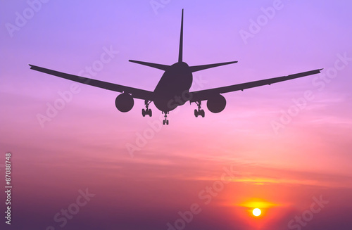 Silhouetted commercial airplane flying at sunset