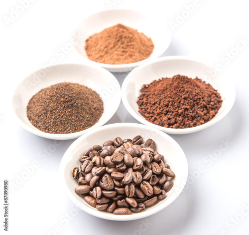 Coffee beans, powdered coffee, chocolate powder and processed tea leaves beverages in white bowl over white background