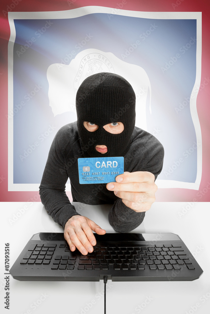 Hacker holding credit card with US state flag on background - Wyoming Hacker holding credit card with US state flag on background - Wyoming