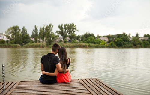 Rear view of a romantic young couple sitting on a jetty.