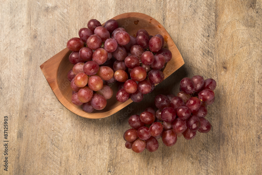Some red grapes in a wooden pot over a wooden surface seen from Some red grapes in a wooden pot over a wooden surface seen from