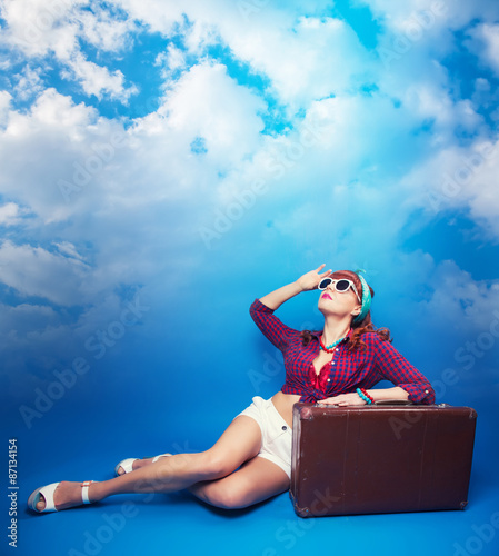 beautiful pin-up girl posing with vintage suitcase against blue