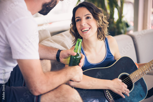 Young couple sitting on a couch with a guitar. The girl is playing the guitar. 