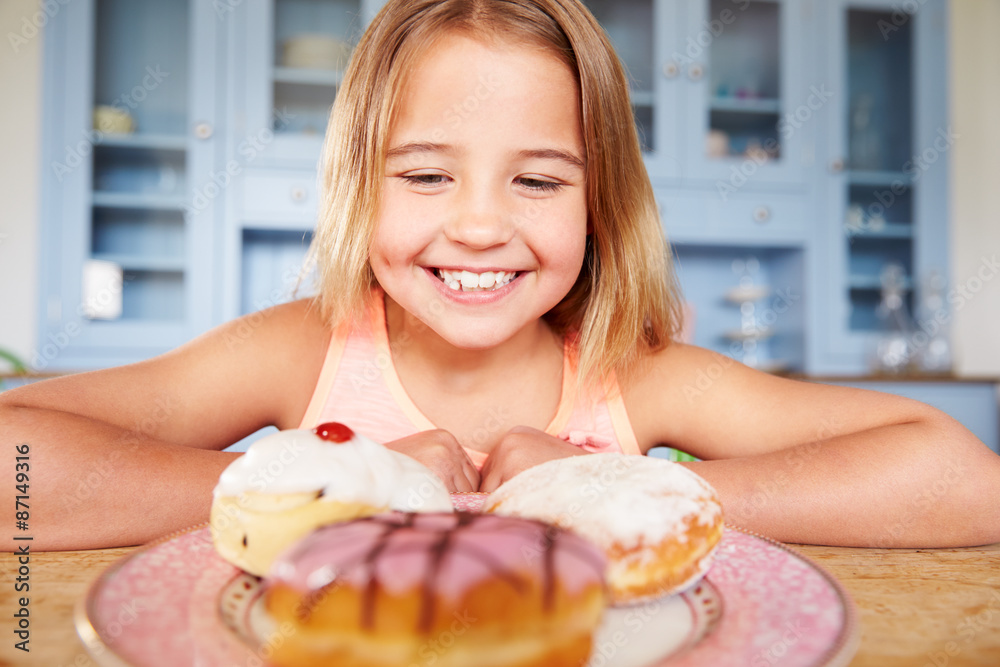 Young Girl Sitting At Table Looking At Plate Of Sugary Cakes Young Girl Sitting At Table Looking At Plate Of Sugary Cakes