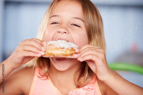 Young Girl Sitting At Table Eating Sugary Donut