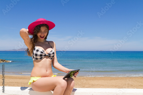 Brunette teen in swimwear enjoys the sun using her tablet.