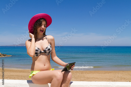 Brunette teen in swimwear enjoys the sun using her tablet.