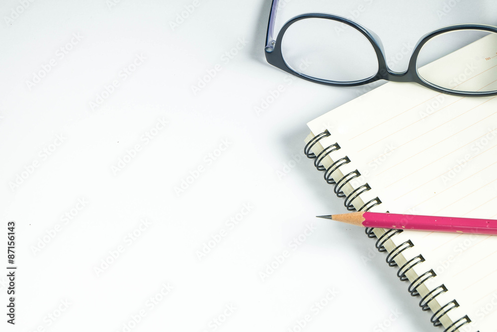 view from above on white desk table with notepad, pencil and eyeglasses view from above on white desk table with notepad, pencil and eyeglasses