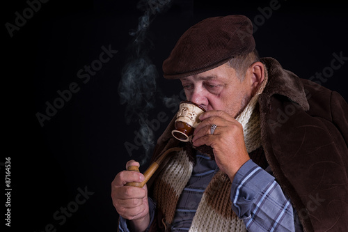 Senior man being chilled to the bone drinks coffee and smokes tobacco-pipe in the darkness