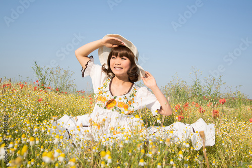Glückliche junge lachende Frau mit Kleid und Hut im Sommer mit Blumen Wiese 
