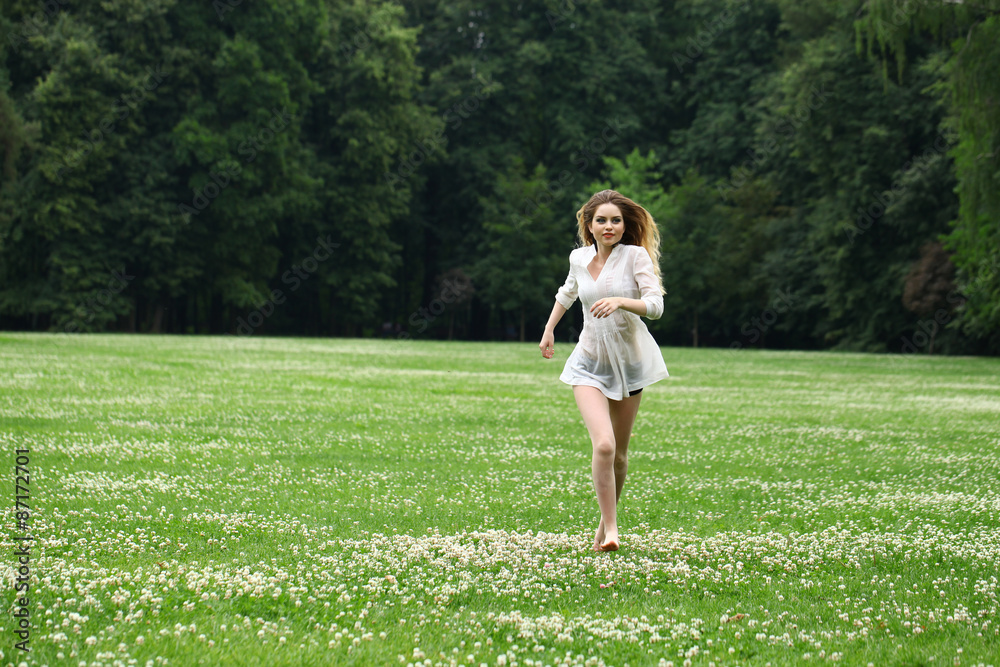 Young beautiful girl in the white shirt is running on the green