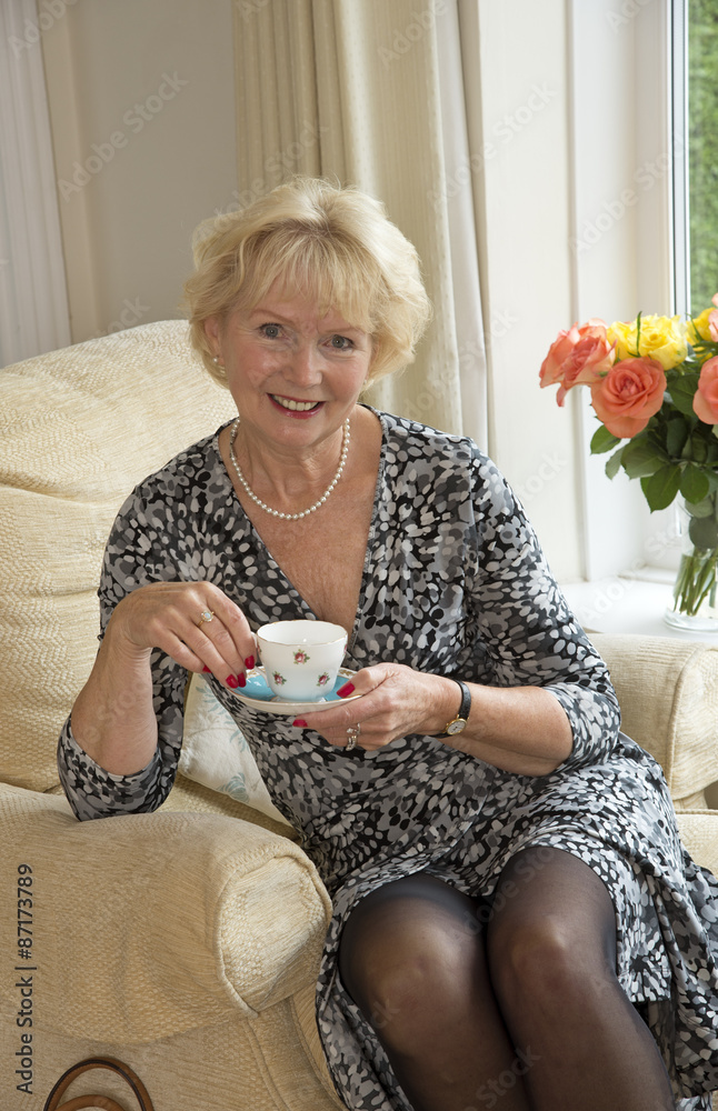 Elderly Woman Sitting In A Comfortable Chair Having A Cup Of Tea Foto