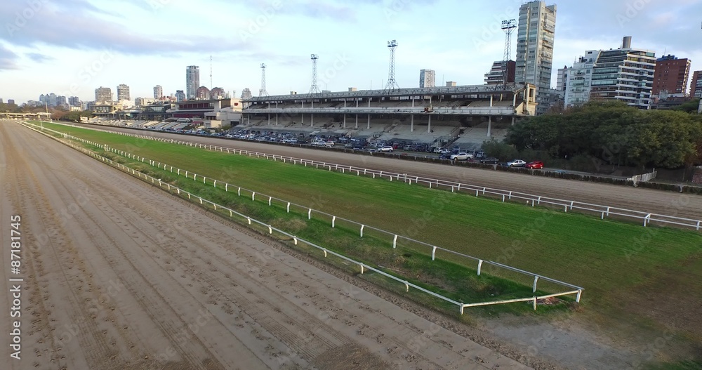 Escena con dron de pista de carreras de caballos, tribunas, estadio y paisaje de la ciudad. Movimiento hacia el estadio desde pista de carreras pasa cerca de iluminación y termina con paisaje urbano
