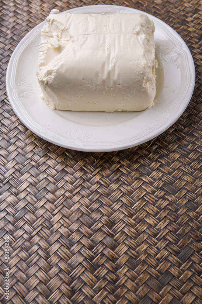 A block of cream cheese on a white plate over wicker background
