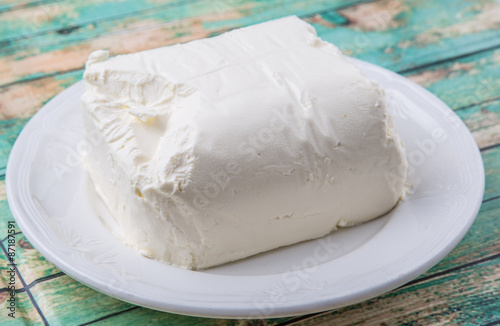 A block of cream cheese on a white plate over weathered wooden background