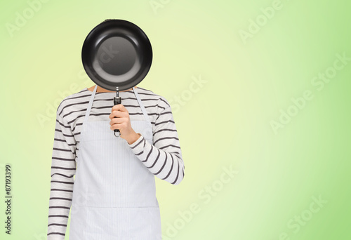 man or cook in apron hiding face behind frying pan © Syda Productions