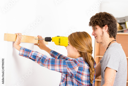 Couple renovating together as man using power drill on wood part and woman helping out by holding