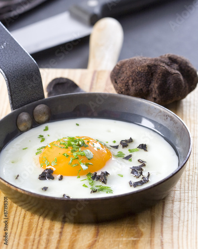 Fried egg with truffle and parsley in a frying pan.