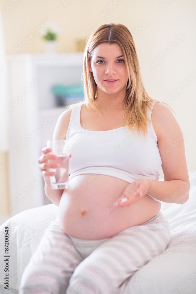Pregnant woman sitting on bed and holding glass of water Pregnant woman sitting on bed and holding glass of water