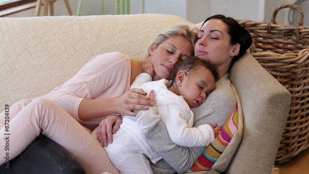 Same sex couple sleeping on their sofa with their baby son sleeping on