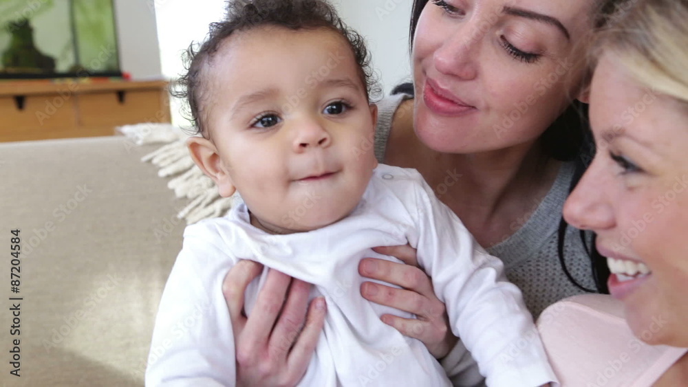 Close up of baby boy being held by his same sex parents. He is interacting with the camera. Close up of baby boy being held by his same sex parents. He is interacting with the camera.