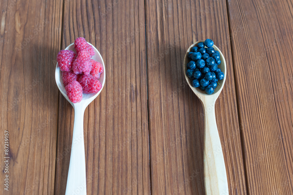 Raspberries and blueberries in spoons on wooden background Raspberries and blueberries in spoons on wooden background