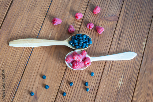 Raspberries and blueberries in spoons on wooden background
