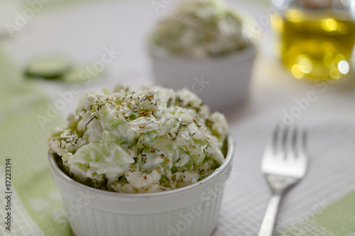 Concept of a vegetarian appetizer, fresh cucumber salad with fresh cottage cheese, garnished with extra virgin olive oil and spices. Set on a white green table cloth.