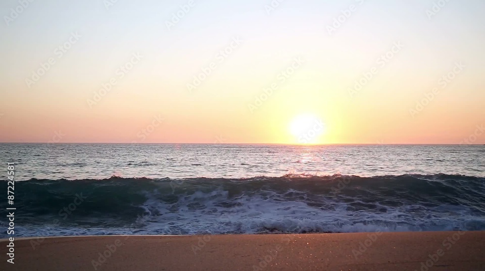 Sunset on horizon ocean line with waves breaking into the sand.