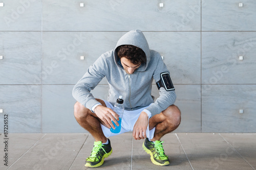 Принти на полотні A young man in sportswear resting in the shade of a building in a summer day, dr