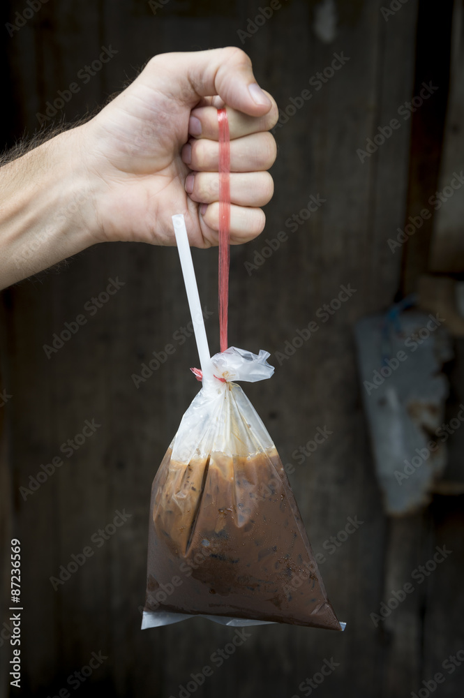Fototapeta premium Hand holding fresh traditional Thai style iced coffee with condensed milk served in a handy plastic bag with a straw