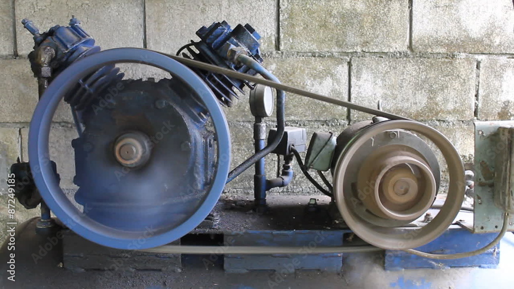 Air compressor is running. Dark blue air pump and motor is running on concrete block background in factory.