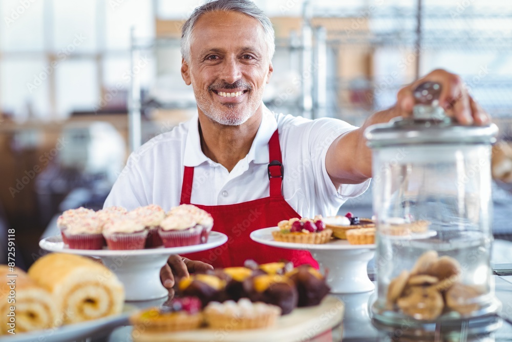 Happy barista smiling at camera behind plates of cakes Happy barista smiling at camera behind plates of cakes