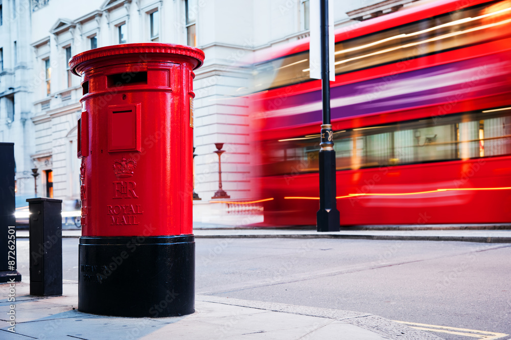 Naklejka premium Traditional red mail letter box and red bus in motion in London, the UK.